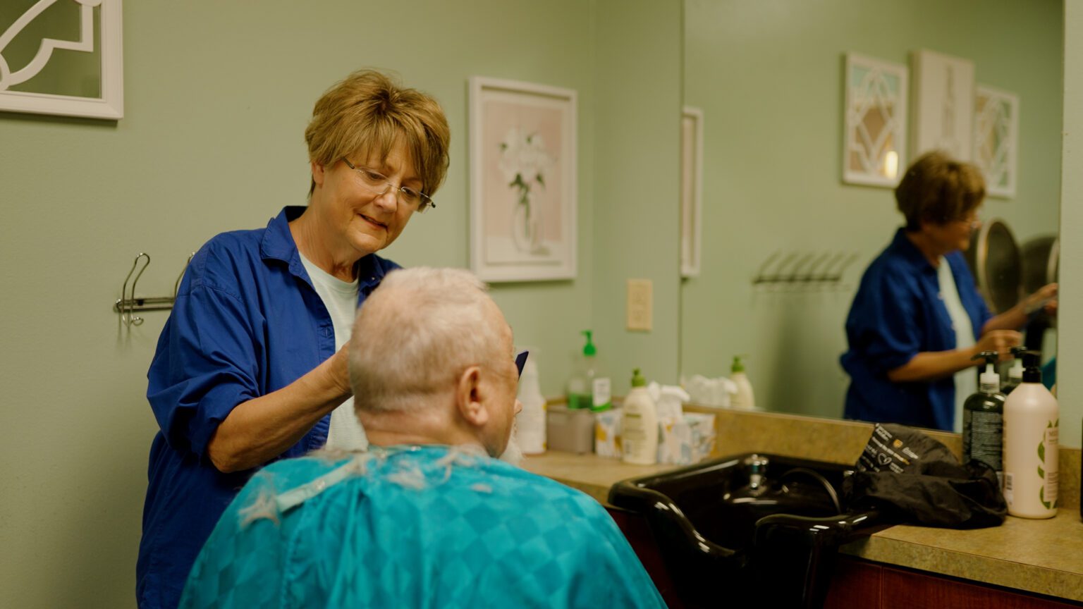 a man gets his haircut by a stylist at a skilled nursing facility